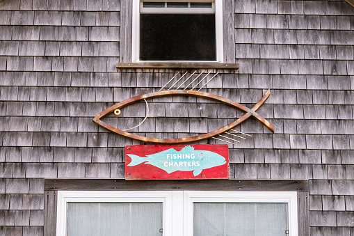 Menemsha, Chilmark, Martha's Vineyard, Massachusetts, US-July 26, 2022: Quaint rustic weathered gray shingled building in iconic fishing village with sign reading fishing charters.