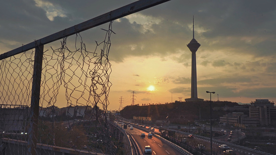 The city of Tehran with a view of the Milad tower behind torn fences during the sunset