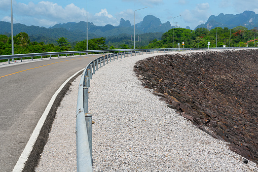 Asphalt road with safety barrier fence of the overpass way above the dam, with scenic beautiful view of mountain as bakground. Transportation and travel scene photo, selective focus.