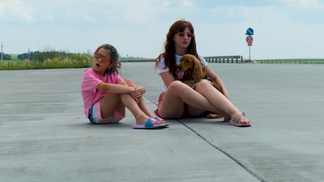 Mom, daughter and dog are sitting on the edge of the highway