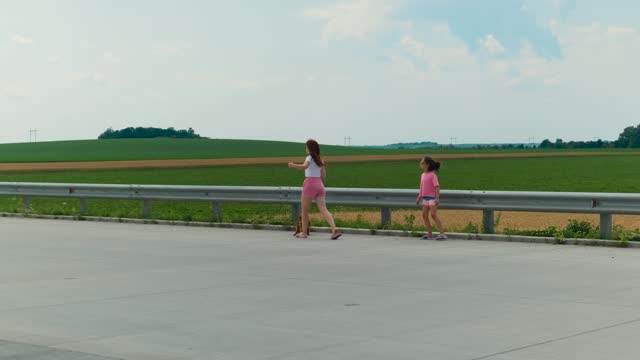 Mom, daughter and dog are walking along the edge of the highway.