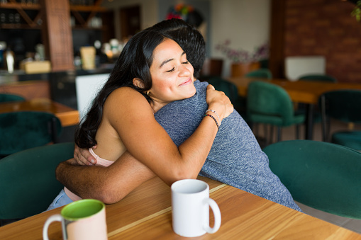 Beautiful young woman hugging her boyfriend and smiling during a romantic date at the coffee shop