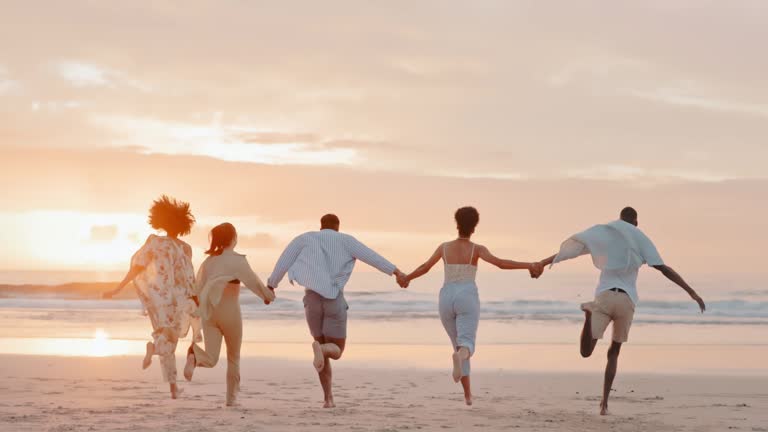 Holding hands, friends or running at beach at sunset for holiday vacation bonding or walking together. Back view, happy or funny group of people playing or relaxing on ocean trip in Miami