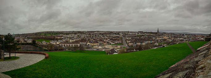 Wide panorama of Derry or Londonderry on a cloudy day viewed from the city walls. Green panorama of the city, residental houses visible.