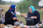 Refugee women and men prepare food outdoors in a refugee camp.