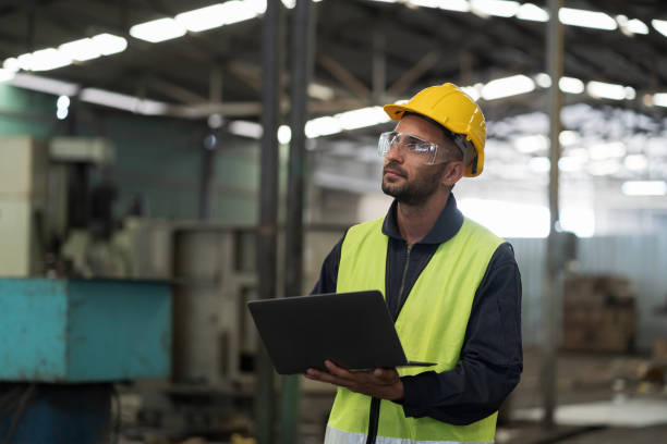 ingegnere maschio che lavora con appunti e macchina di controllo in fabbrica. operaio maschio che lavora con la macchina cnc con uniforme di sicurezza, casco nella fabbrica dell'industria - inspector built structure engineer clipboard foto e immagini stock