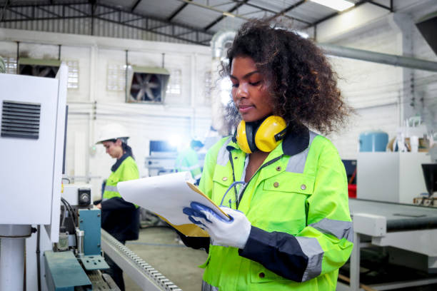 African industrial woman worker with curly hair wears safety vest, writes on file folder document, female engineer check and maintenance machinery at CNC woodworking manufacturing furniture factory. una trabajadora industrial africana con cabello rizado usa chaleco de seguridad, escribe en el documento de la carpeta de archivos, la ingeniera revisa y la maquinaria de mantenimiento en la fábrica de muebles de fabricación de madera cnc.