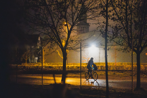 Silhouette of an unknown man on a bicycle commuting in early morning or late night. Commuter on a bike with  backpack.