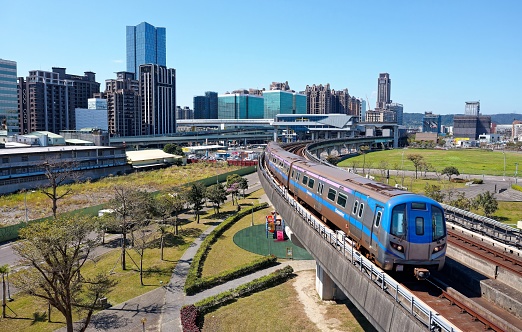 A metro train of Taoyuan Airport MRT travels on the elevated railway track, with high rise buildings booming in the Industrial Park in background, in Xinzhuang District, New  Taipei City, Taiwan, Asia