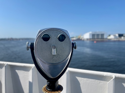 Binocular telescope on a rotating base mounted on an outdoor touristic viewpoint with blurred cityscape on a background. Black and white photo