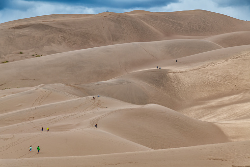 Alamosa, United States - August 19, 2022:  Various groups of tourists hiking into the tallest sand dunes in North America at Great San Dunes National Park in Colorado, USA.