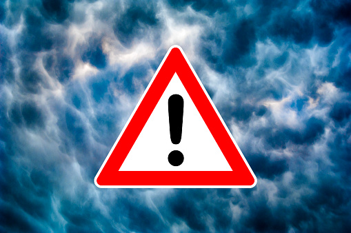 Pictogram of warning triangle with exclamation mark against dramatic under weather sky as symbol for severe weather warning