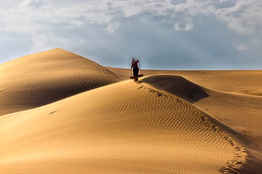 A woman wearing casual clothes and conical hat walk on top of Nam Cuong sand dunes in Phan Rang Province South of Vietnam.