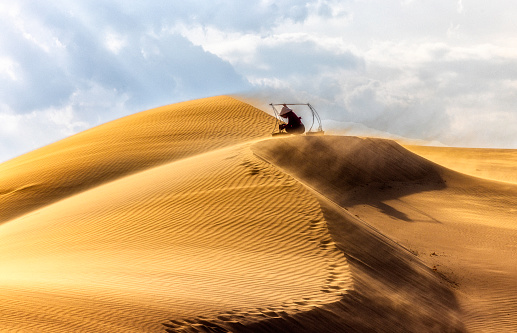 A woman wearing casual clothes and conical hat sit on top of Nam Cuong sand dunes in Phan Rang Province South of Vietnam.