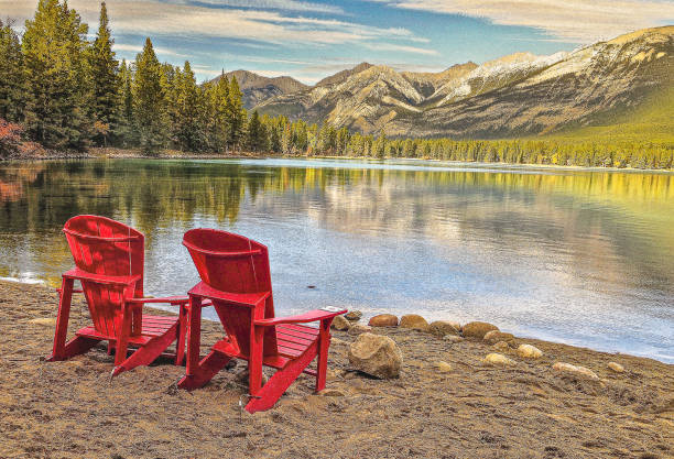 istock Two red deck chairs rest along a lake reflecting snow capped mountains 1545912642