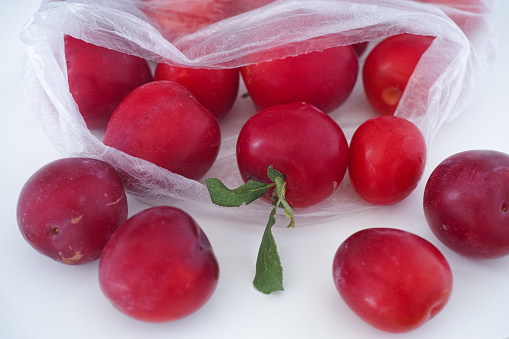 Ripe red plums rolling out of a plastic bag. Close up.