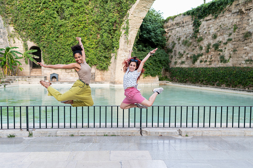 Photo with copy space of happy friends jumping on a park next to a pool. Next to the cathedral of Mallorca. The arch of the Drassana