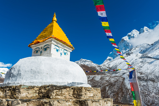 Brightly coloured Buddhist prayer flags fluttering in the thin mountain air beside traditional white washed stupa high in the Everest National Park, Himalayas, Nepal.