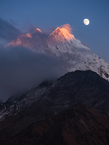 Moon rising over the jagged snow capped peaks of Thamserku 6608m soaring high in the Himalayan mountains of Nepal.