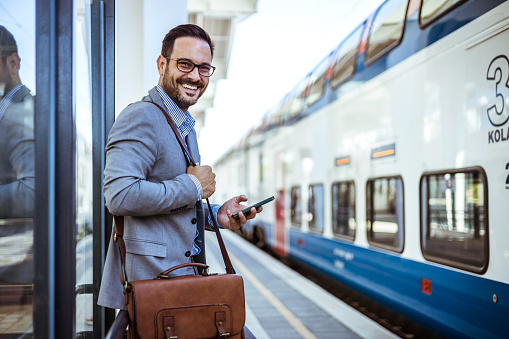 Busy bearded businessman traveller using smartphone at public station. Every travelling entrepreneur needs a virtual assistant. Businessman holding smartphone while at the train station and the train is arriving.