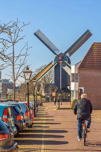 Leiden, The Netherlands - March 5, 2022: A man is cycling across the Kort Galgewater towards windmill De Put in Leiden on a sunny day