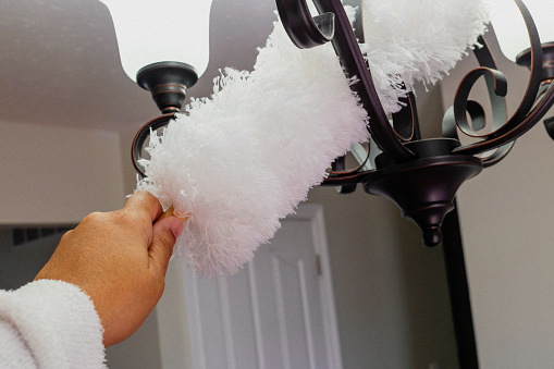 A black woman using a duster on a light fixture