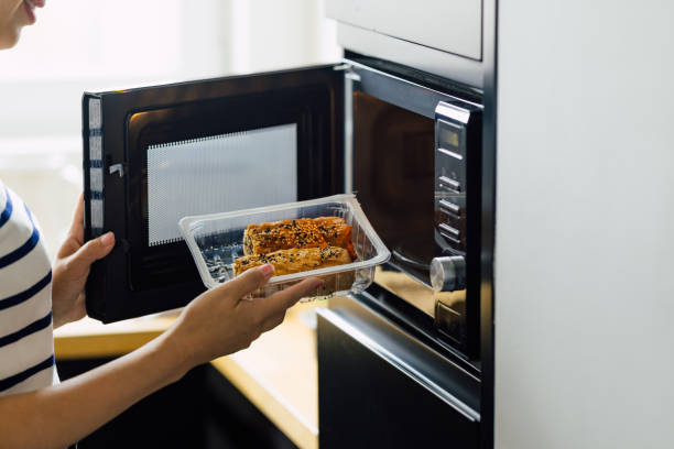 Anonymous Woman Making a Meal in a Microwave Oven An unrecognizable woman reheating a meal in a microwave oven. convenience food stock pictures, royalty-free photos & images