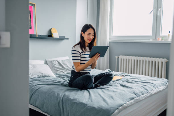 istock Beautiful Asian Woman Sitting on her Bed and Talking on a Video Call, Using a Tablet 1546278126