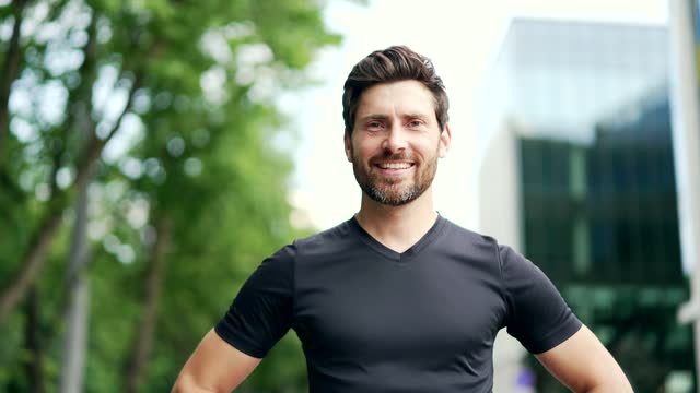Portrait of happy bearded handsome sporty man in black t-shirt looking at camera.