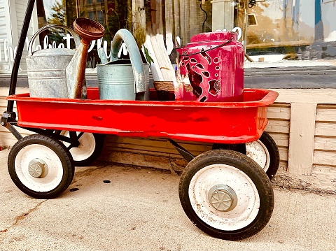 A little red wagon filled with antique gardening tools including watering cans