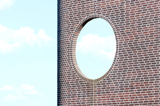 Brick wall with round window against blue sky background