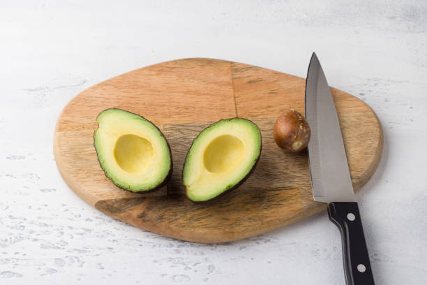 istock Fresh avocado cut in half and avocado pit with a knife on a wooden board on a light gray background, top view 1546577318