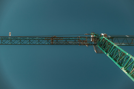 A green crane gracefully suspended against a clear sky, its slender silhouette cutting through the air, symbolizing the breakthrough of industrialism