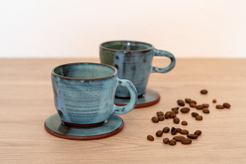 Two coffee espresso cups with saucers and coffee beans on a wooden table