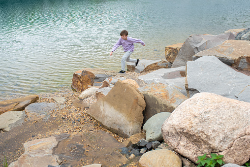the child runs, jumps from stone to stone on a journey on a summer morning. happy child on vacation in nature, runs along a mountain lake on a cloudy day.