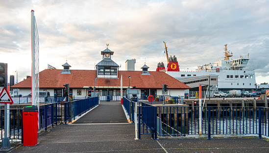 Rothesay, Scotland, UK - 13th July 2023: The Ticket Office at the Ferry Terminal on Rothesay, Isle of Bute in the Firth of Clyde, Scotland, UK. The Cal-Mac ro-ro ferry MV Argyle (Earra Ghàidheal) is moored for the night at the terminal, and there are various parked vehicles.