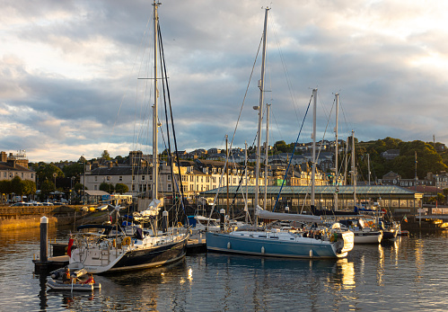 Rothesay, Scotland, UK - 13th July 2023: A group of yachts moored in the harbour in Rothesay, Isle of Bute. Some people are enjoying an evening on the deck of a Hanse 400 charter cruiser and a man is rowing an inflatable dinghy in which a boy is a passenger.