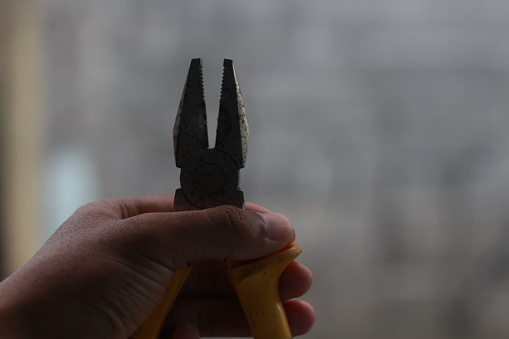 The hand of a man is holding a black yellow pliers isolated on the blur background