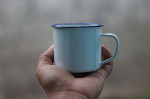 Close-up of male hand holding steel mug sprayed with water. Outdoors background of blurred