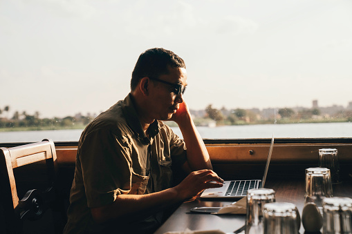 Businessman using laptop while sitting by window in passenger boat