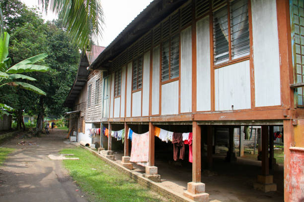an old traditional malay wooden house raised off the ground on wooden stilts and with wooden walls and louvred windows in the village of hulu langat, selangor state, malaysia and with laundry hanging underneath the house to protect it from the rain. - louvred imagens e fotografias de stock