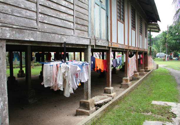 an old traditional malay wooden house raised off the ground on wooden stilts and with wooden walls and louvred windows in the village of hulu langat, selangor state, malaysia and with laundry hanging underneath the house to protect it from the rain. - louvred imagens e fotografias de stock