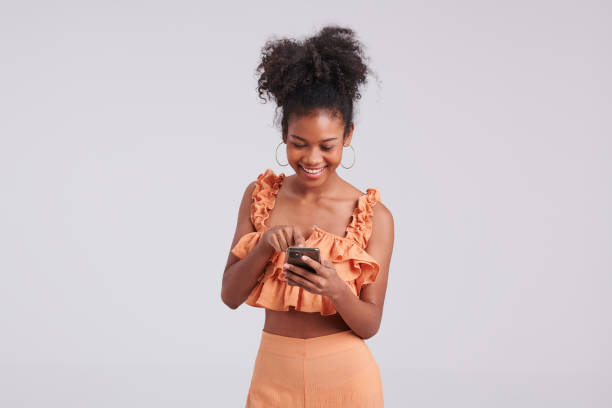 istock Smartphone Glamour: Black Girl in Orange Shirt Perfects Studio Pose 1547120579
