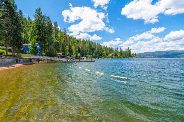 View from the public beach of waterfront homes, marina and the mountains surrounding Carlin Bay, one of the bays on Lake Coeur d'Alene, in Coeur d'Alene, Idaho, in the North Idaho Panhandle. Carline Bay is located on the eastern shore of Coeur d'Alene Lake in the Bitterroot Range of the Rocky Mountains. vista desde la playa pública de las casas frente al mar, el puerto deportivo y las montañas que rodean carlin bay, una de las bahías en el lago coeur d'alene, en coeur d'alene, idaho, en el norte de idaho panhandle. carline bay se encuentra en la costa