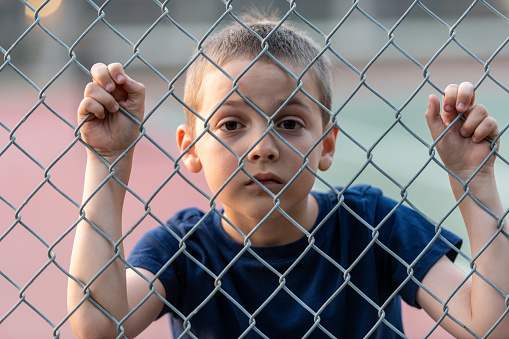 Sad little boy looking through a fence