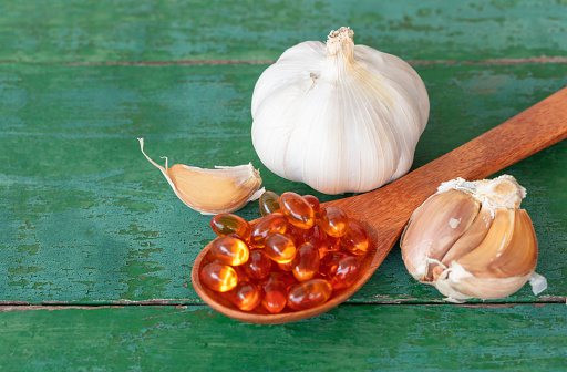 Garlic bulbs, garlic cloves, capsules of oil extract in wooden spoon, and on old green wooden background, Garlic can help reduce the risk of many diseases. Classified as healthy food.