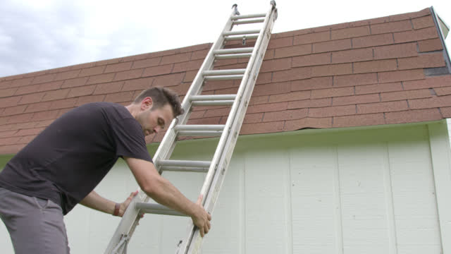 Man Setting up an Extension Stepladder to Climb on the Rooftop of a Shed