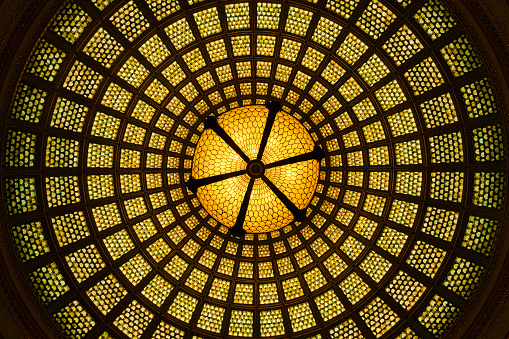 Unique perspective view of the world’s largest Tiffany glass-domed ceiling, centered by a Tiffany glass chandelier hanging from the dome itself.  Located in the Preston Bradley Hall of the historic Chicago Cultural Center.   Photo taken looking up from the center of the majestic hall.