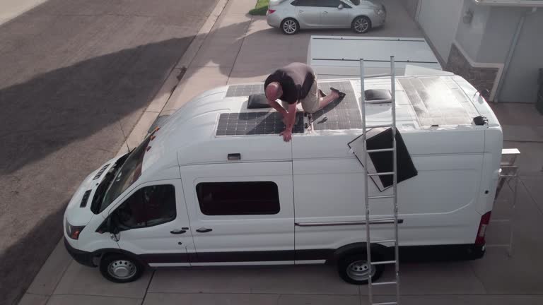 Jib-Style Shot of a Mature Man Cleaning Dirt off a Set of Solar Panels On Top of Camper Van