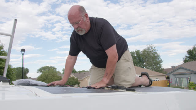 Mature Man Using a Wet Rag to Clean Solar Panels on a Camper Van